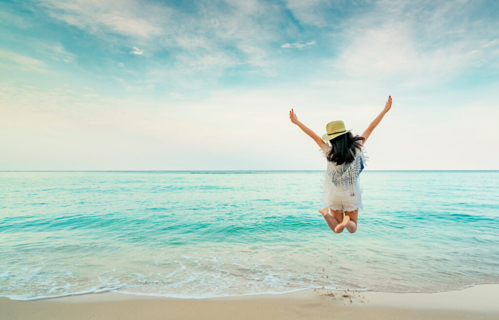 A young woman jumping for joy on the beach after having a MILD procedure.