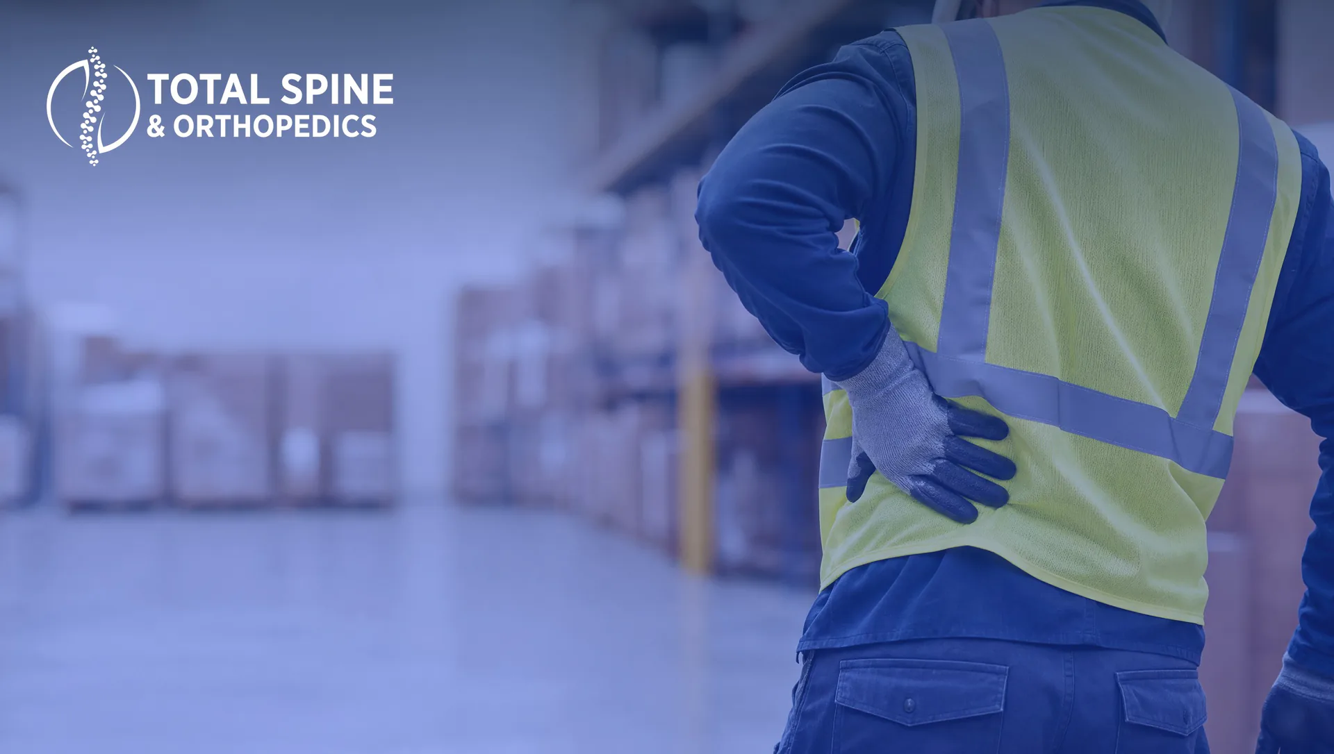 Worker in a safety vest gripping his lower back in a warehouse